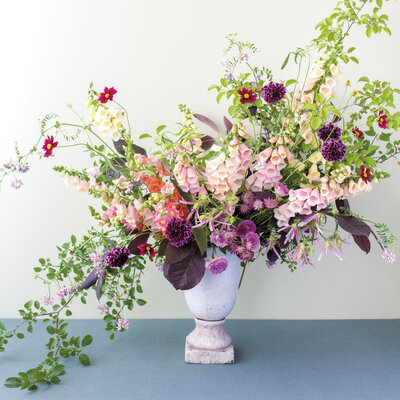 A cascading arrangement of bright spring flowers sits in an urn on a blue floor.
