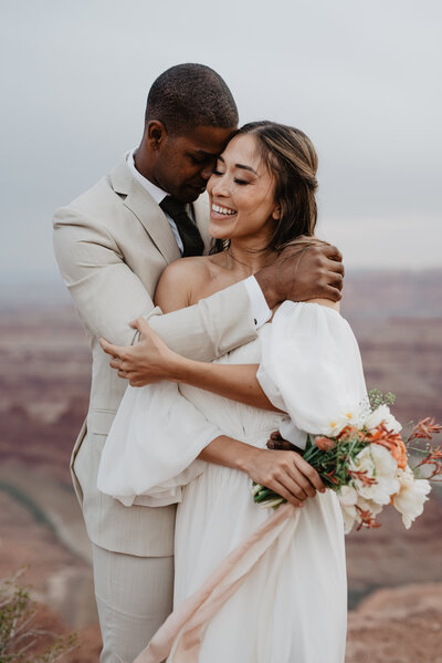 utah elopement photographer captures outdoor bridal with man holdin ghis bride by the shoulder and leaning his head against hers for their arches national park wedding photos