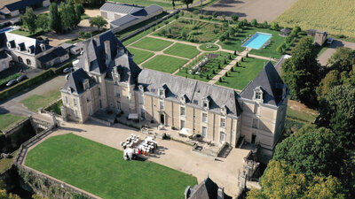 An aerial view of Morgan and Felix's wedding ceremony at a French chateau, highlighting the elegant setup, lush gardens, and historic architecture.