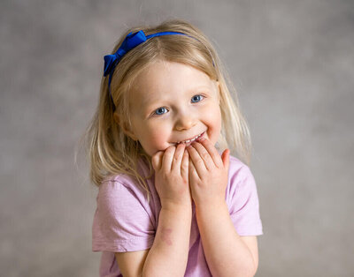 A preschool girl giggles and smiles as she  plays with her shirt during a school photo day that captures authentic child personalities and expressions.