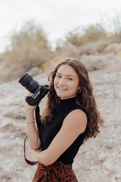 Phoenix wedding photographer, Kaylie Miller holding her camera smiling at the Salt Flats.