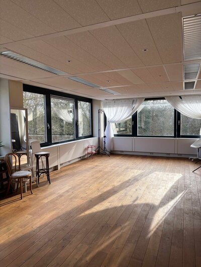 Daglichtstudio van Isabeau Bosscher Fotografie, een grote open ruimte met houten vloer en grote ramen.