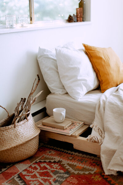 Stack of books and a coffee mug next to a neatly made bed