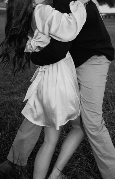 In the midst of an engagement session in a picturesque field, a guy affectionately holds his arms around a girl