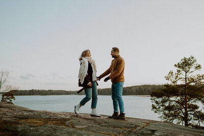 Pari seisoo rantakalliolla kädet yhdessä ja nainen on astumassa miestä kohit Kivenlahdessa Espoossa