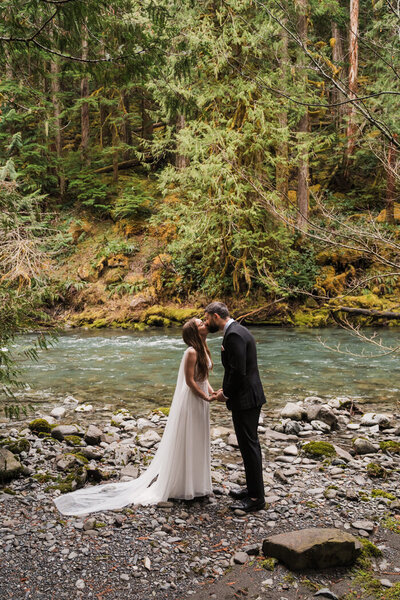 bride and groom kiss along a turquoise river in olympic national park