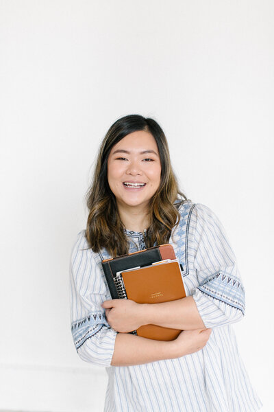A woman smiling while holding an iPad and a notebook.