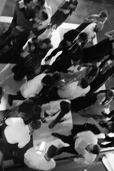 A look down from above a busy dance floor during a wedding in black and white