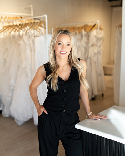 Emily smiling headshot by Julia Haus photography. She is wearing a black suit at J Bridal and leaned against the front reception desk.