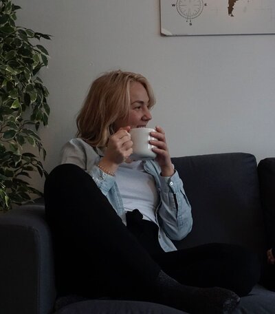 mielen paremminvoinnin ja kehomieliyhteyden valmentaja istuu sohvalla pitäen kahvikuppia k'ädessään  hymyillen