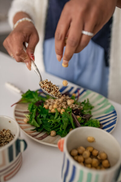 Woman sprinkling chickpeas on a green leafy salad with a striped plate