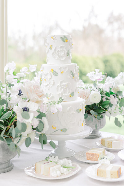 a three-tiered white wedding cake with flowers on cake stand