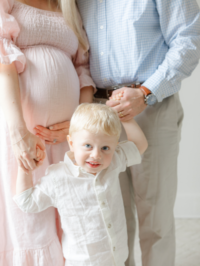 pregnant woman holds baby bump and smiles at camera during boston maternity photoshoot