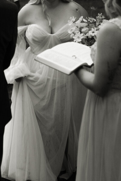 Officiant reads scripture from the Bible during an intimate wedding ceremony as the bride and groom listen.