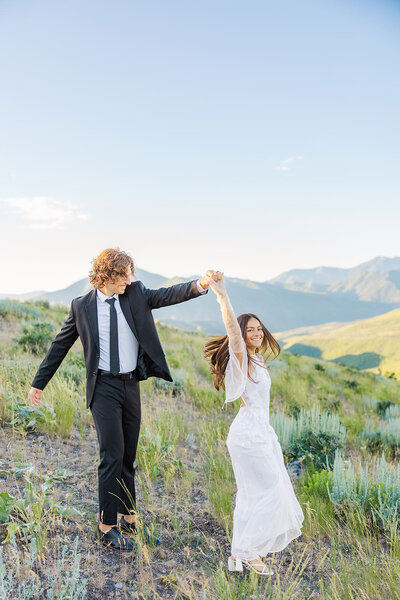 Bride and groom in their wedding attire twirling at Deer Creek Overlook in Utah, capturing a romantic moment against a stunning mountain backdrop.