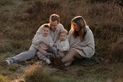 ouders zitten met hun zoontjes op een kleedje en lachen met elkaar 