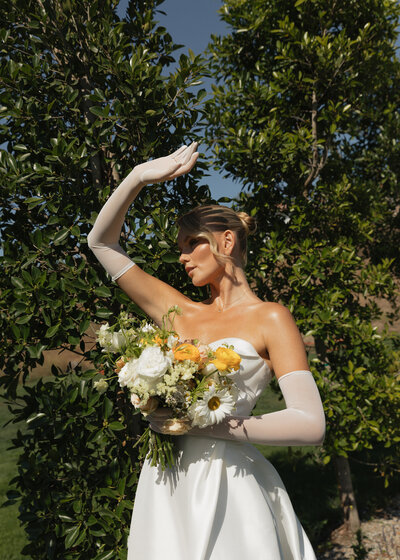 bride in full sunlight holding her hand up towards the sun and holding her bouquet outside villa balbiano in italy.