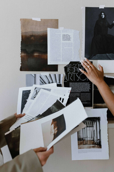 Hands holding photographs and magazine pages and taping them to a moodboard on a wall