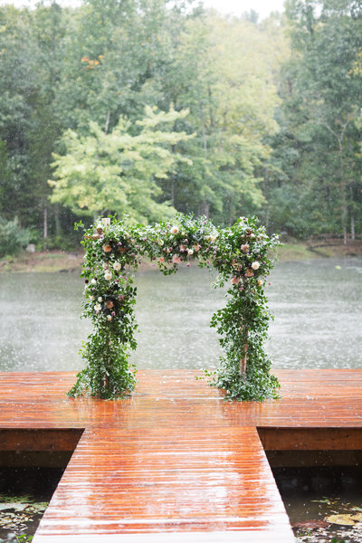 large chuppah with flowers and greenery on a dock with a lake and woods by roots floral design