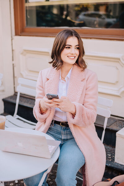 Madison sitting at table outside with laptop on iphone smiling
