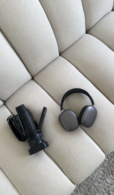 Flat lay of professional camera and luxury headphones on neutral couch, representing elevated content creation tools for social media brands