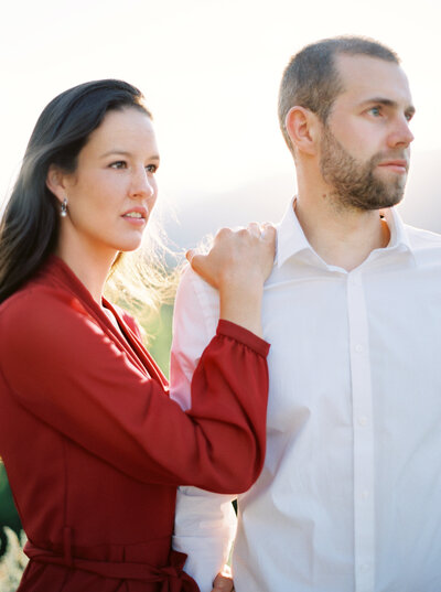 Woman in red top holds husbands shoulder and looks off into the distance