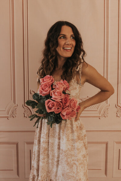 Claire smiling in a floral dress while holding a bouquet of pink roses