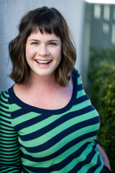 Commercial acting headshot for Katie Adams, smiling, wearing green and blue striped shirt.