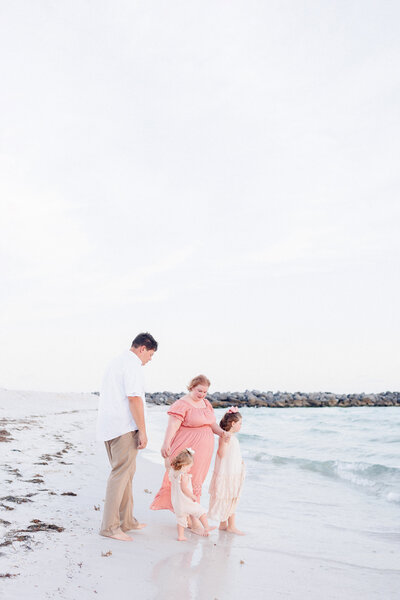 A family of four standing on the beach at sunset looking at the water at St. Andrews State Park.