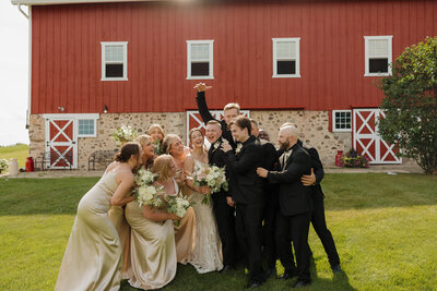 bride and groom celebrate on their wedding day surrounded by their wedding party at folk song farm in richfield, wisconsin 