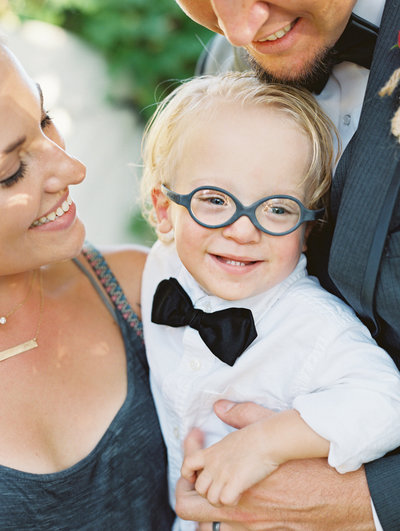 A family smiles at their little boy wearing blue glasses during a family session with Ventura County photographer Daniele Rose