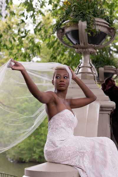 Editorial portrait of a black bride holding her veil while resting at the Bow's Bridge.