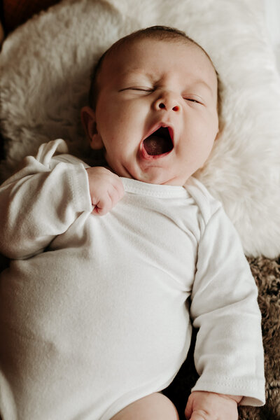 Yawning baby photographed in moody studio in Annapolis Maryland wearing white.