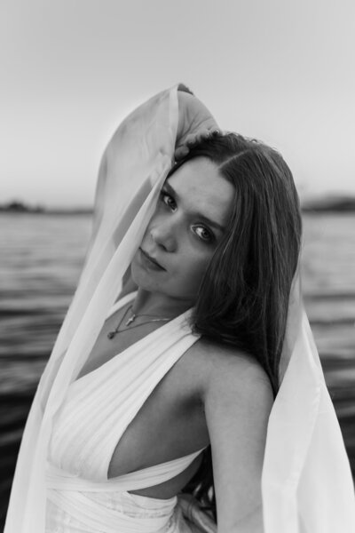 Striking black and white portrait of a bride in a flowing white wedding dress and veil, gazing seriously at the camera, captured in a dramatic and timeless bridal session by a Portland and destination wedding photographer.