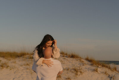 Michaela of Michaela Crawford Photography is laughing while her husband holds her up in the air on the beach in Santa Rosa Beach, FL. 