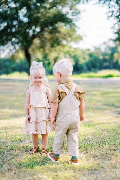 Little boy and girl standing in the grass smiling at each other