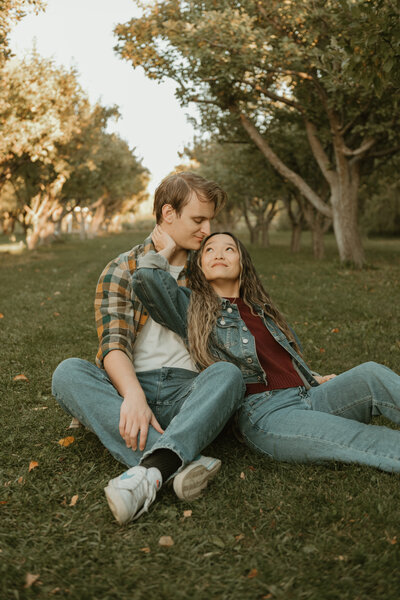 Couples photoshoot taken by Bailee Freeman Photography at the BYUI apple orchards. Couple laying on the green grass and looking up towards each other with apple trees lining the background.