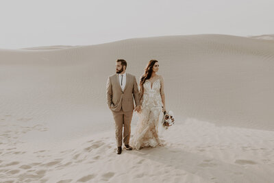 Happily eloped couple staring off into opposite directions at Utah Sand Dunes. Desert wedding attire. Boho Wedding. 