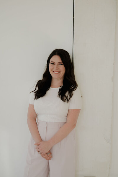 Wedding planner in WI, CJ, poses in white t-shirt and blush pink pants with her hands held together in front of her.