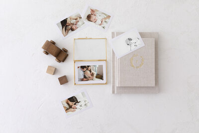 Flatlay of printed newborn and family photos, heirloom keepsake boxes, and linen albums from a Kansas City newborn photographer’s product collection.