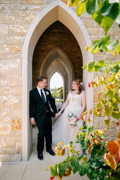 Bride leaning on groom’s shoulder with bouquet in front of white building