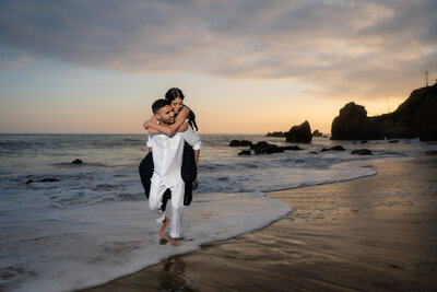 Indian bride and groom couple eloping at Malibu's El Matador State Beach during sunset golden hour with vibrant sky colors.