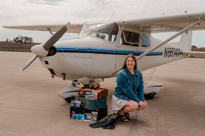 Teenage girl in kneels next to luggage in front of a plane.