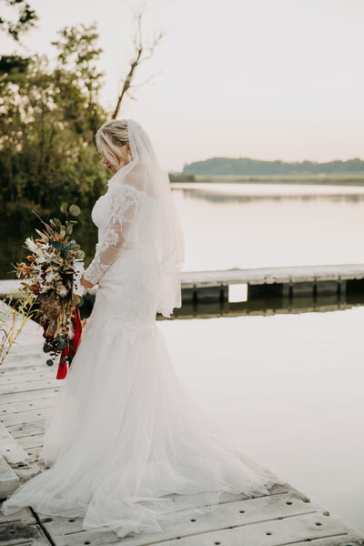 Lillian holding her bridal bouquet, standing on the dock over a pond during her sunset bridal portraits after her wedding ceremony at Navy Lakes in Millington, Tennessee.