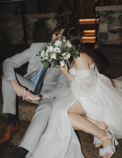 bride and groom sitting together and kissing behind bouquet
