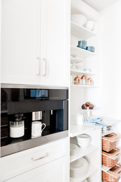 Bright and organized kitchen with built-in coffee machine, open shelves displaying white dishes and copper jars, and a countertop with muffins and coffee mugs, symbolizing efficiency and simplicity in creating systems that work seamlessly