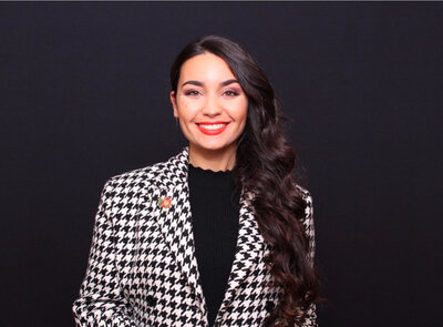 Woman in a black-and-white houndstooth jacket smiling in front of a charcoal gray background.