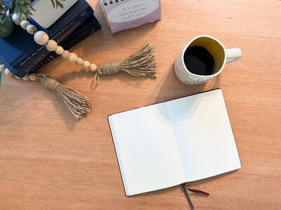 Top-down view of journaling setup with open notebook, coffee mug, beads, and motivational calendar.