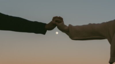 Blue hour shot of a couple holding hands under a glowing moon, silhouettes framed by soft desert light