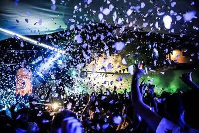 Fans at an outdoor music festival  dance  with lights and confetti